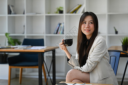 积极的亚洲女商务人士坐在她的工作场所喝咖啡图片