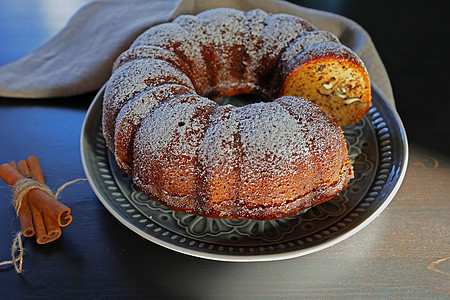 Bundt 蛋糕在深色木质背景下的质朴盘子上撒上糖粉 选择性聚焦 盘子上的圆形棕色焦糖和坚果蛋糕图片