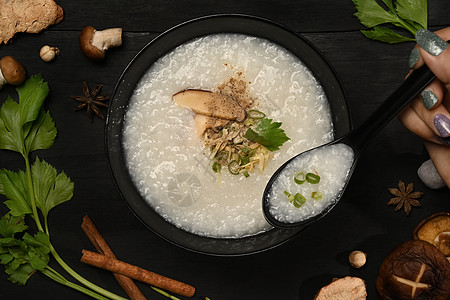 传统中国大米粥 配有蘑菇 姜粉和切片炒菜 在黑木制桌边煮黑鸡汤 用于健康早餐图片