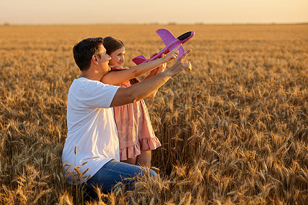 在小麦田里玩玩具飞机对抗天空的可爱女孩喜悦孩子童年乐趣男人蓝色女儿场地父亲家庭图片