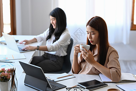 青年女商务人士早上在她的办公桌喝咖啡 她正在喝酒图片