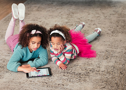 变得丰富多彩和富有创意 两个小女孩在家里一起玩数字平板电脑的高角度拍摄图片