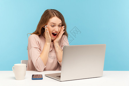 情感年轻女性在蓝背景的笔记本电脑上工作博主商务震惊互联网成功视频惊喜惊愕电话屏幕图片