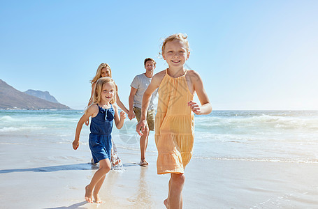 快乐的年轻家庭有两个孩子在沙滩上奔跑 享受一个有趣的暑假 两个精力充沛的小女孩在赛跑 而他们的父母则在后面跟着图片