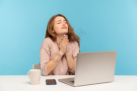 情感年轻女性在蓝背景的笔记本电脑上工作办公室商务自由职业者失败祷告蓝色饶恕上帝帮助人士图片