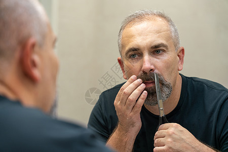 中年英俊男子用剪刀剪胡须和修整外形隔断灰色镜子浴室胡子头发男人刮胡子男性成人图片