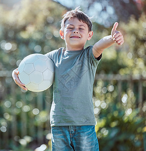 一个可爱的小男孩在外头举着足球球 抬起大拇指的镜头被射中了 -你看到了吗?图片