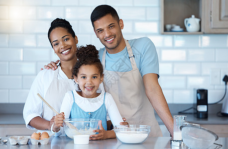 一个充满爱心的西班牙裔家庭在家里一起烘烤的肖像 可爱的小女孩在父母的帮助下在厨房里混合配料图片