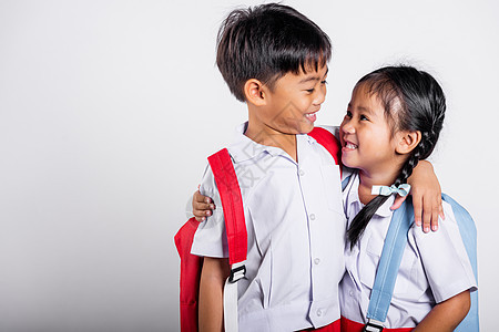 两个亚洲学生孩子女孩男孩小学生兄弟姐妹微笑快乐穿着学生泰国制服红色裤子裙子互相拥抱编织男生手足友谊背包衬衫女性朋友青少年教育图片