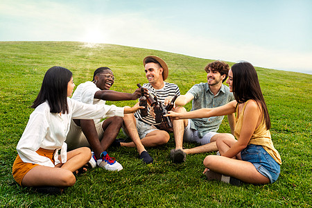 一群多种族快乐的朋友在公园的草地上喝着啤酒 享受着令人愉快的烤面包图片