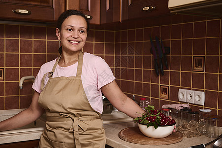 迷人的女性美食者站在厨房的柜台顶上 笑着看在家庭厨房的一旁图片