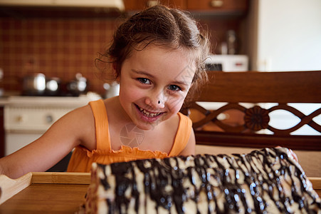 可爱的白人小女孩看着摄像头 后面有一片模糊的樱桃巧克力馅饼 在生锈舒适的木制厨房里图片