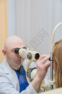 一名男性眼科医生用光束检查一个使用现代装置的年轻女孩的视力 该装置带有光束视网膜治疗测量考试器材测试医疗诊断眼睛女士图片