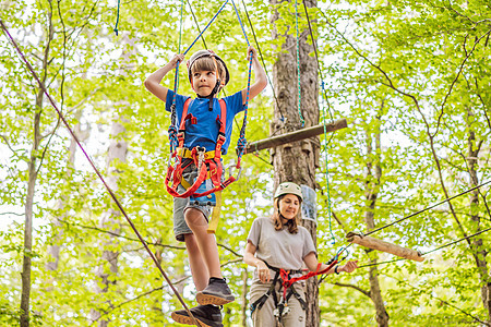 母亲和儿子在森林中的极端公路手推车滑索中攀登 在树上的登山扣安全连接到树顶绳索冒险公园 家庭周末儿童儿童活动概念男人金属绳索森林图片