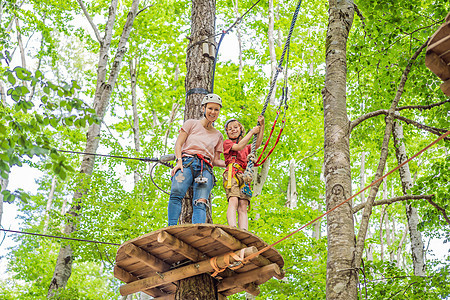 母亲和儿子在森林中的极端公路手推车滑索中攀登 在树上的登山扣安全连接到树顶绳索冒险公园 家庭周末儿童儿童活动概念森林平衡绳索女士图片