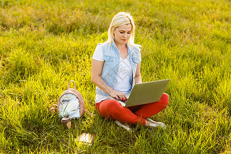夏日用笔记本电脑拨打视频电话时 坐在公园绿草地上 双腿交叉的年轻美女肖像笔记黑发教育青少年女性杯子耳机女孩学生女士图片