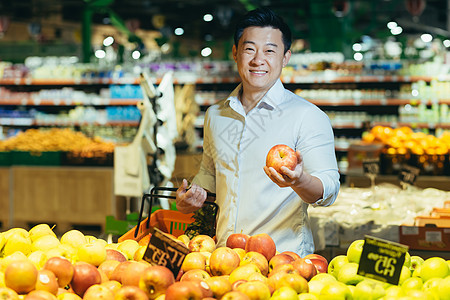 亚洲超市买家的肖像 男人选择苹果水果 然后放进篮子图片