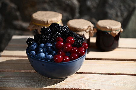 在各种模糊果酱背景的木盒子上配有成熟樱桃 蓝莓和黑莓的陶瓷碗图片
