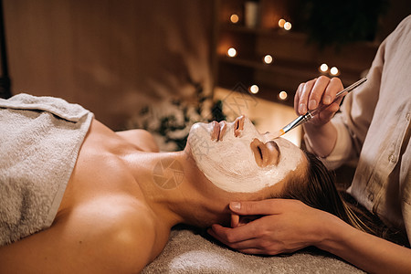 美容学家用面具遮住妇女的脸面 以恢复皮肤的活力服务打扫女士程序美容院皮肤科美容师奶油沙龙病人图片