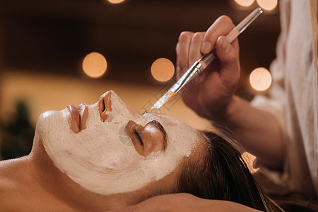 美容学家用面具遮住妇女的脸面 以恢复皮肤的活力美容皮肤科女孩清洁病人打扫医生黏土营养护理图片