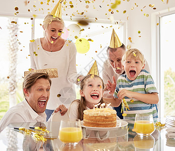 欢快的世代幸福家庭戴着派对帽 在家里用五彩纸屑和蛋糕庆祝小女孩的生日 兴奋的孩子 父母和祖父母享受特别惊喜活动图片