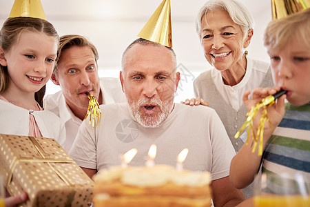 老人在家里和家人一起庆祝生日 戴着派对帽 吹着口哨 爷爷吹灭生日蜡烛 在孙子 妻子和儿子的簇拥下许愿图片