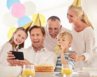一个幸福的家庭在聚会上庆祝生日 戴着帽子 用手机自拍 成熟的男人在聚会上为他的父亲 妻子和孩子拍照 同时留下特别的回忆图片