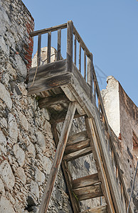 在蓝天背景下 通往一座历史建筑屋顶的旧木楼梯 风化的楼梯和复古石墙背景 观看风景并呼吸新鲜空气的地方图片