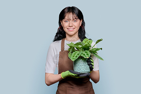 穿着围裙手套 带着灰色孤立背景的陶工厂微笑的年轻女子工作植物群女士花园快乐职业女性花店植物商业图片