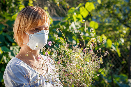戴保护面罩的妇女持有野花花束 并试图与过敏作斗争发烧公园流感鼻子干草季节性面具季节花粉女士图片