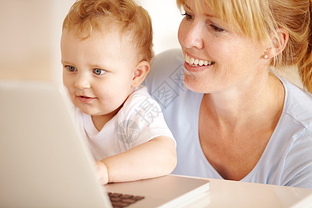 美丽的母亲在笔记本电脑上 帮她那小男孩打字的宝贝儿子打字图片