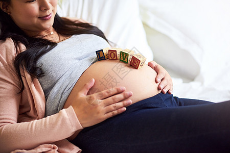 一位怀孕妇女躺在地上 家里肚子上有木质婴儿砖头 她正在回家的路上享受幸福图片