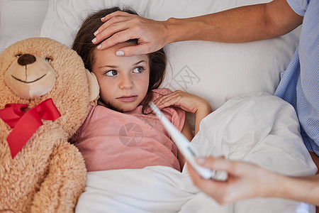 生病的小女孩和她的泰迪熊躺在床上 而她的母亲则用温度计测量她的体温 年轻的单亲父母坐在生病的孩子身边 摸着她的额头 小孩子在妈妈图片