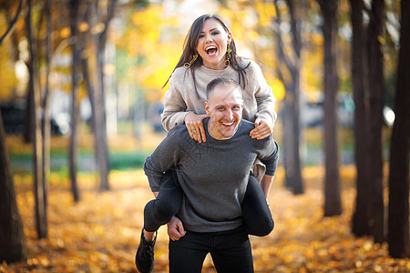 一个快乐的男人带着一个笑女人 背着他去享受最后的温暖阳光明媚的秋天图片