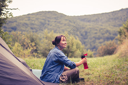 妇女在帐篷附近的山上 是可喜的远足者运动闲暇成人娱乐活动远足旅游女性背包图片