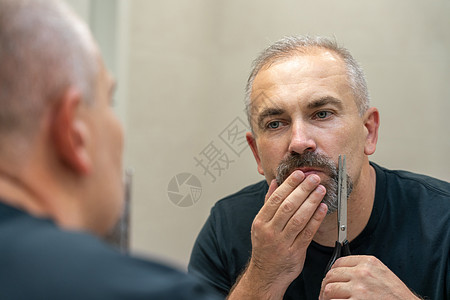 中年英俊男子用剪刀剪胡须和修整外形成人刮胡子灰色浴室男性镜子胡子男人头发隔断图片