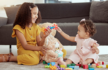 可爱的混血儿在家里的客厅里和小妹妹玩耍 两个可爱的西班牙裔小女孩坐在一起玩玩具和毛绒玩具时亲密无间 微笑的兄弟姐妹图片