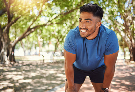快乐的混合种族男子站在公园里 双手放在膝盖上微笑着 西班牙裔男性在跑步后休息 健康男人对自己在户外锻炼时的表现感到满意图片