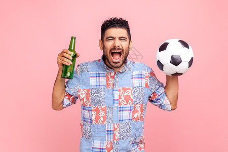疯狂的影迷穿着蓝色散装衬衫 欢乐地尖叫着庆祝赢得他最喜欢的球队 握在手球和酒瓶上图片