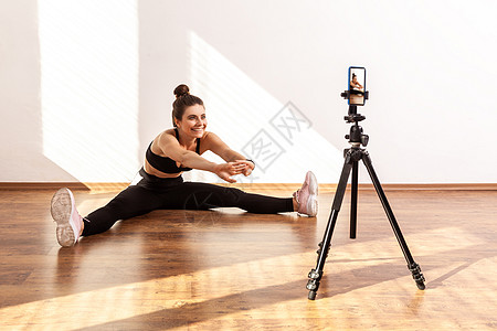 女在线培训员使用三脚架电话记录锻炼后伸展的辅导课 以记录其内容图片