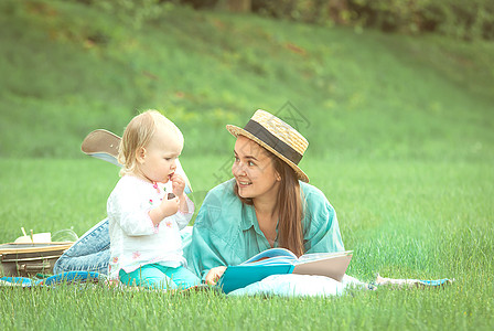 童话书母亲正在给睡在公园草地上的女婴读书童话童年乐趣女儿喜悦女孩孩子快乐婴儿家庭背景