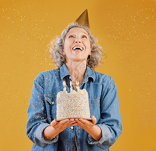 一位快乐的成熟白人女性戴着生日帽 拿着蛋糕 而五彩纸屑从上方落在工作室的黄色背景下 微笑的白人女士庆祝又一年食物幸福帽子退休蜡烛图片