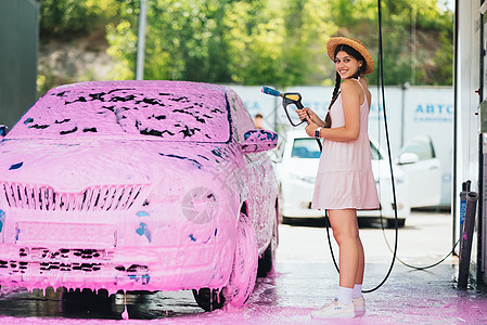 用粉色泡沫覆盖的汽车装着水管的水龙头的妇女肥皂洗车成人打扫女性头发女士软管工作黑发图片