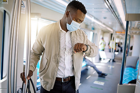 独自旅行的黑人商务人士 一位年轻的非洲裔美国商务人士站在火车上 一边看手表上的时间 一边戴着口罩去城里图片