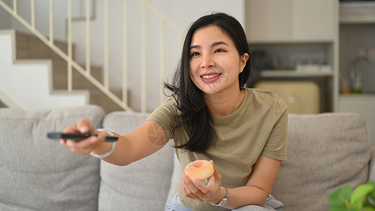 带遥控器的年轻亚洲女性在家看搞笑电视喜剧电影图片