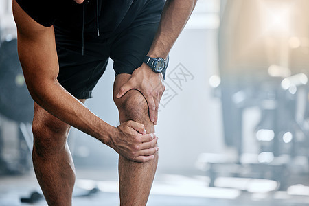 不知名的教练独自在健身房 膝盖受伤 一位教练在运动健身俱乐部锻炼时站立和揉腿 健身中心一名男子在日常训练中感到疼痛图片
