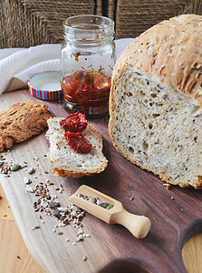 一条自制的全麦面包和一块木砧板上的切片面包 种子和全谷物的混合物 一罐晒干的西红柿放在新鲜面包皮上 健康食品理念早餐木板脆皮乡村图片