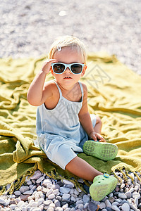 小女孩调整了太阳镜 坐在沙滩的毯子上图片