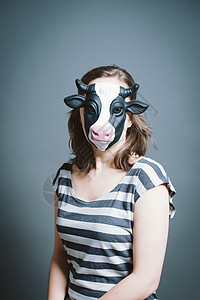 在工作室用灰色背景戴面罩的年轻妇女奶牛条纹性格面具展示女士概念动物冒充女性图片