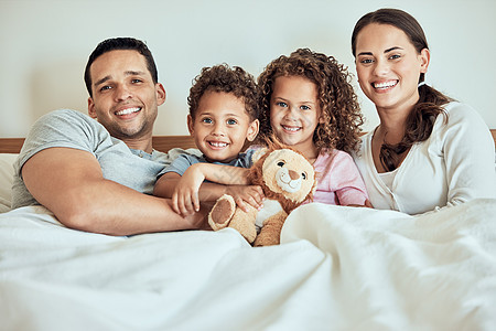 躺在床上的幸福家庭的画像 微笑的西班牙裔家庭躺在床上休息 父母在家里与孩子建立联系 兄弟姐妹和他们的父母一起放松 兄妹带着泰迪熊图片